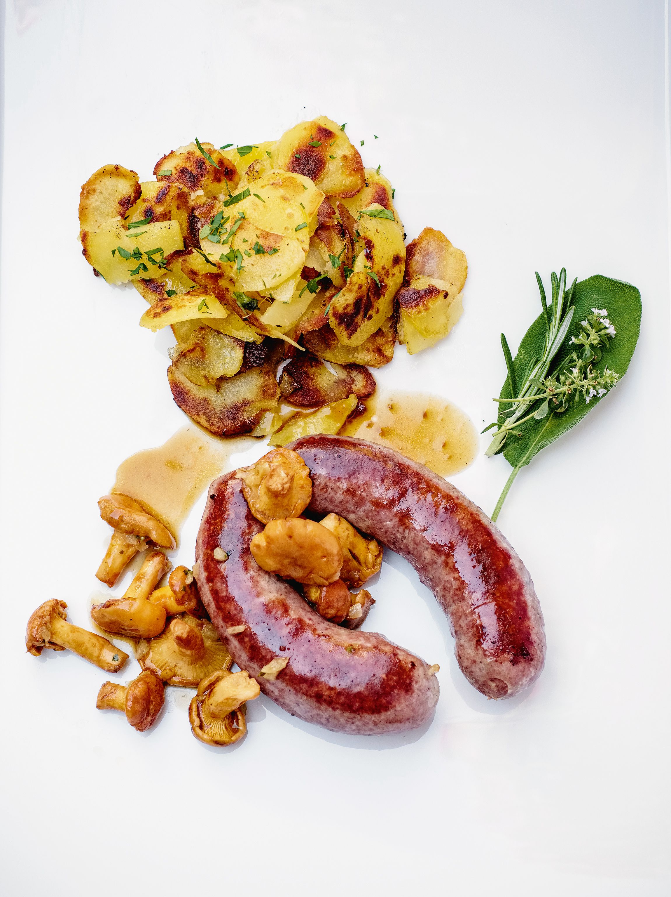 Ein Teller mit gerösteten Kartoffeln, Wurst, Pilzen und einem Kräuterzweig.
