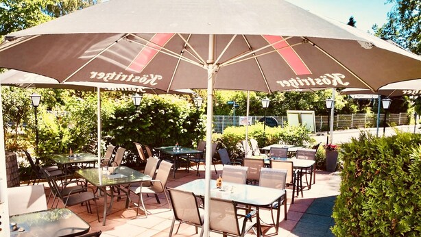 An outdoor patio area with tables and chairs under umbrellas, surrounded by greenery. - Hotel Villa Fröhlich (Ostseebad Baabe)