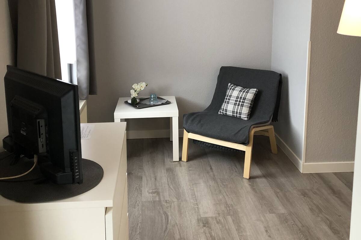A room with a desk, a chair, a lamp, and a television.