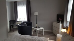 A modern hotel room with a bed, a desk, a chair, a lamp, a TV, and a window with curtains. - Hotel Villa Fröhlich (Ostseebad Baabe)