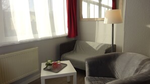 A room with a radiator, a white table with a tray of flowers, a grey armchair, a striped sofa, and a lamp. - Hotel Villa Fröhlich (Ostseebad Baabe)