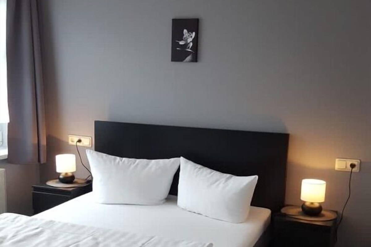 A neatly made bed with white linens, a dark headboard, and two bedside tables with lamps.
