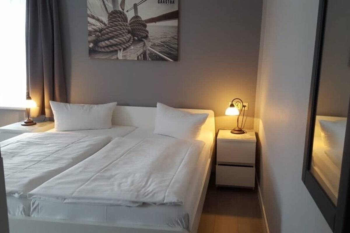 A hotel room with two beds, a nightstand with a lamp, a framed picture on the wall, and a mirror.