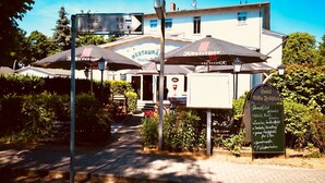 A restaurant with outdoor seating, a sign indicating directions to nearby towns, and a sign listing hotel amenities. - Hotel Villa Fröhlich (Ostseebad Baabe)