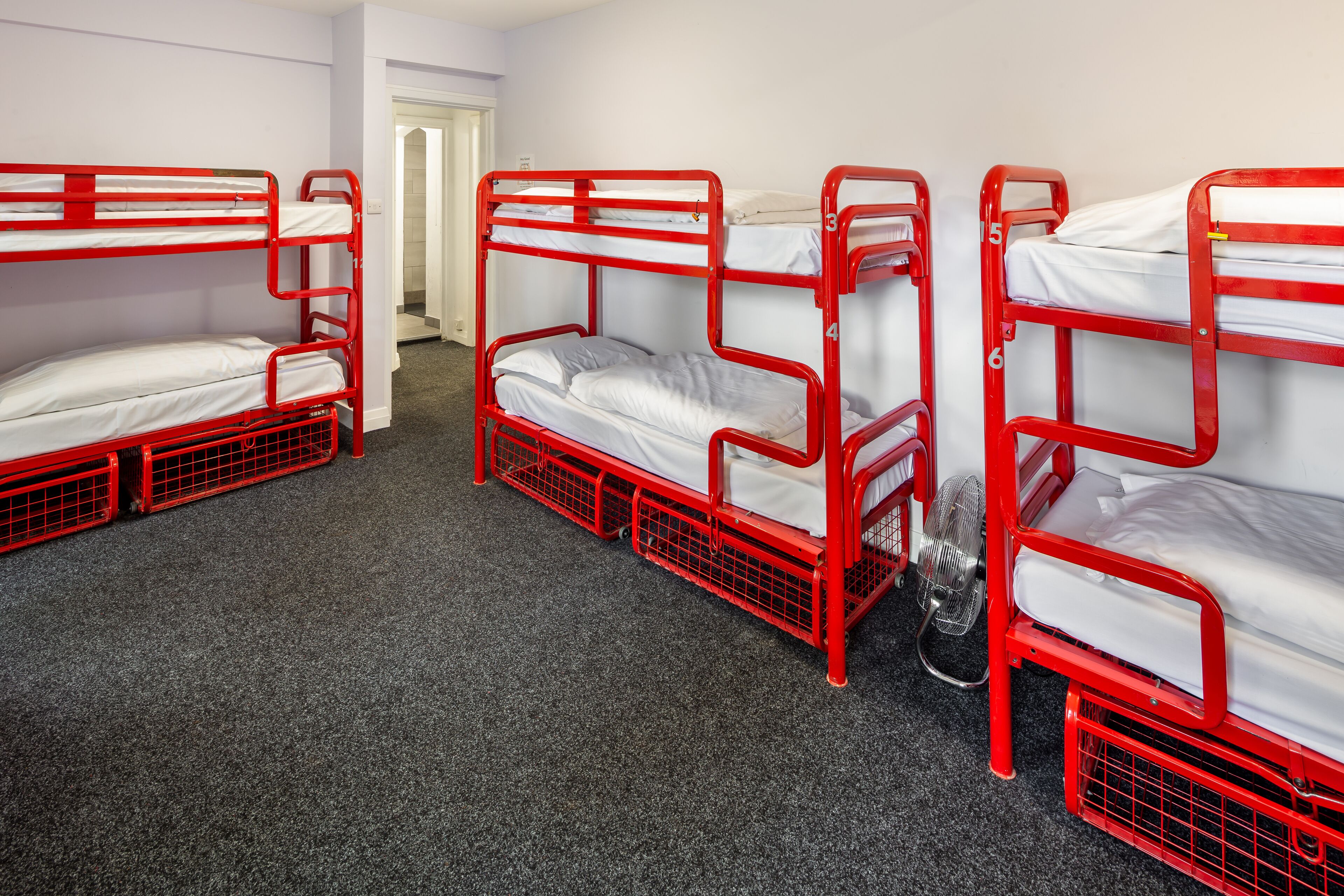 A room with four red bunk beds arranged in a row, carpeted floor, and a door leading to another room.