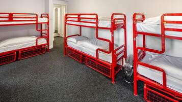 A room with four red bunk beds arranged in a row, carpeted floor, and a door leading to another room.
