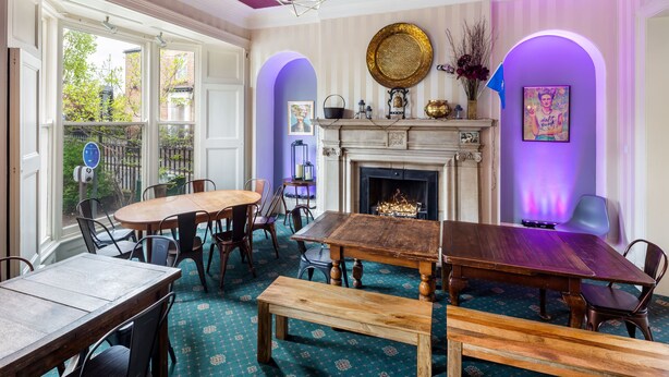 A dining area with a fireplace, a round table, and a bench. - Astor York - Hostel (York)