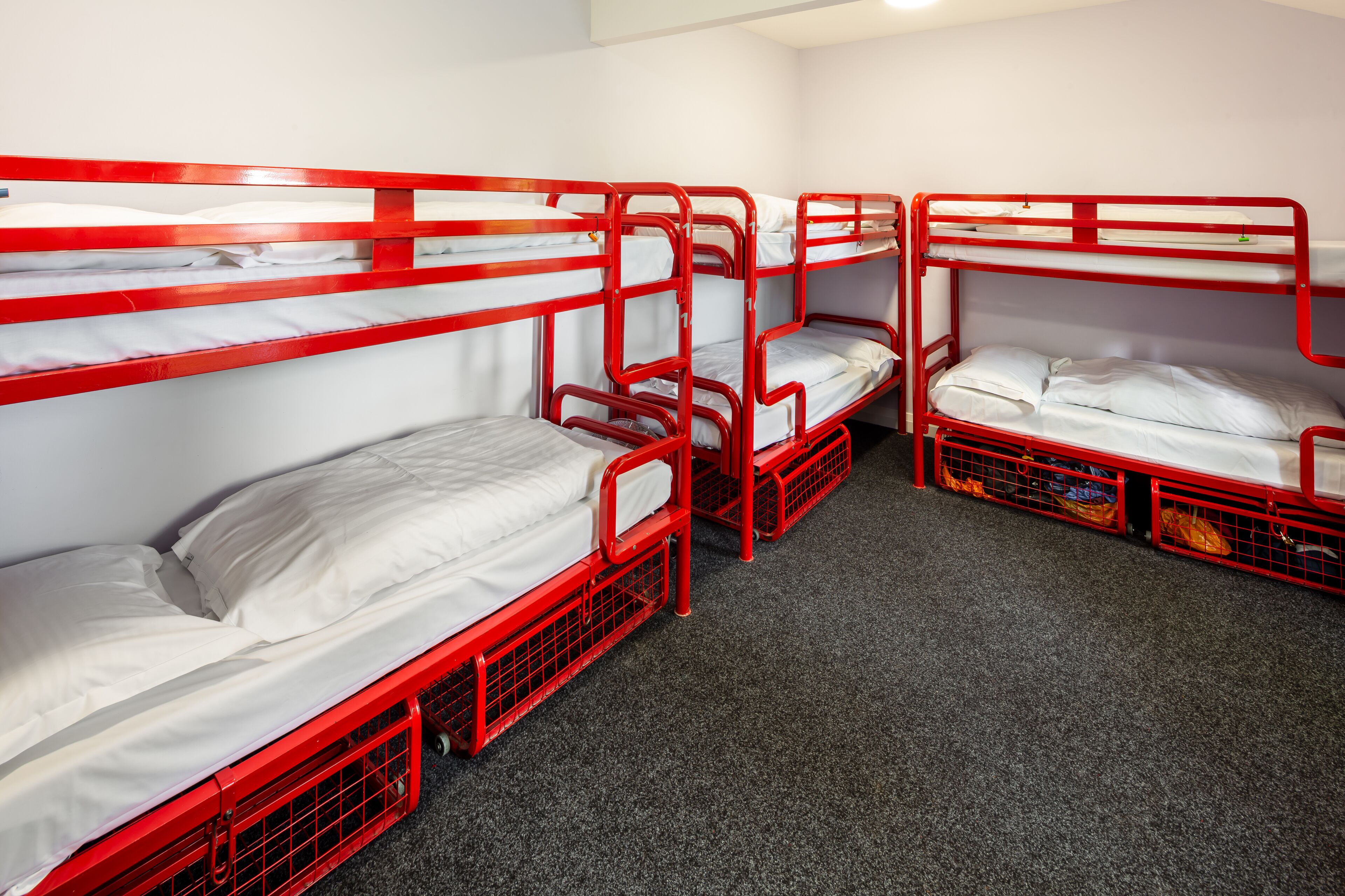 A room with four bunk beds, each with a mattress and pillows, arranged in a row.