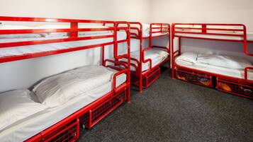 A room with four bunk beds, each with a mattress and pillows, arranged in a row.