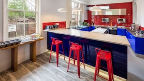 A modern kitchen with a central island, red bar stools, and a view of the outside through large windows. - Astor York - Hostel (York)