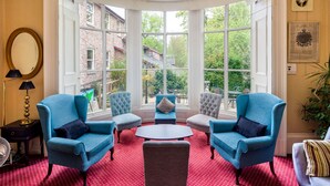 A room with a bay window, blue armchairs, a round table, and a red patterned carpet. - Astor York - Hostel (York)