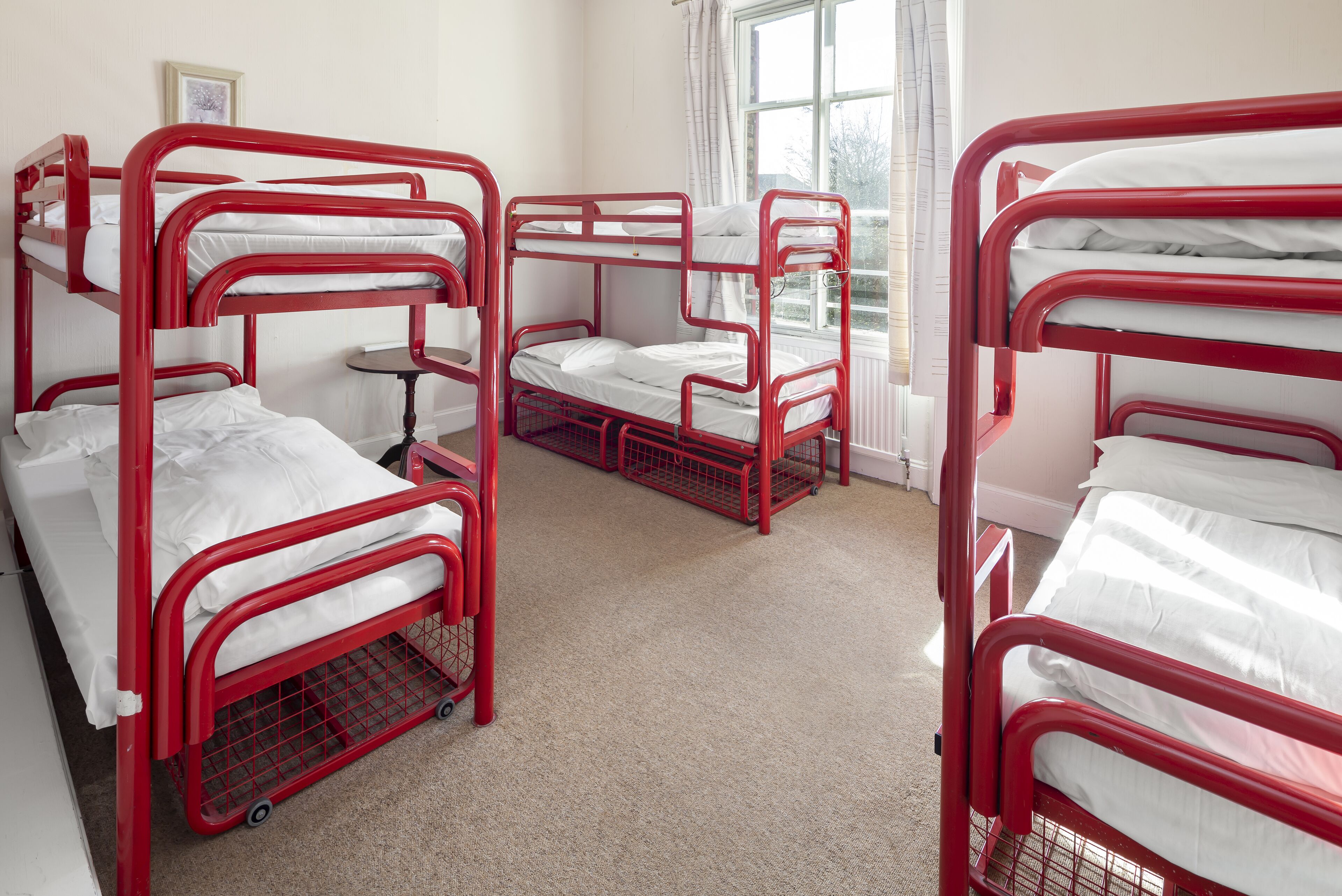 A room with bunk beds, a small table, and a window with curtains.