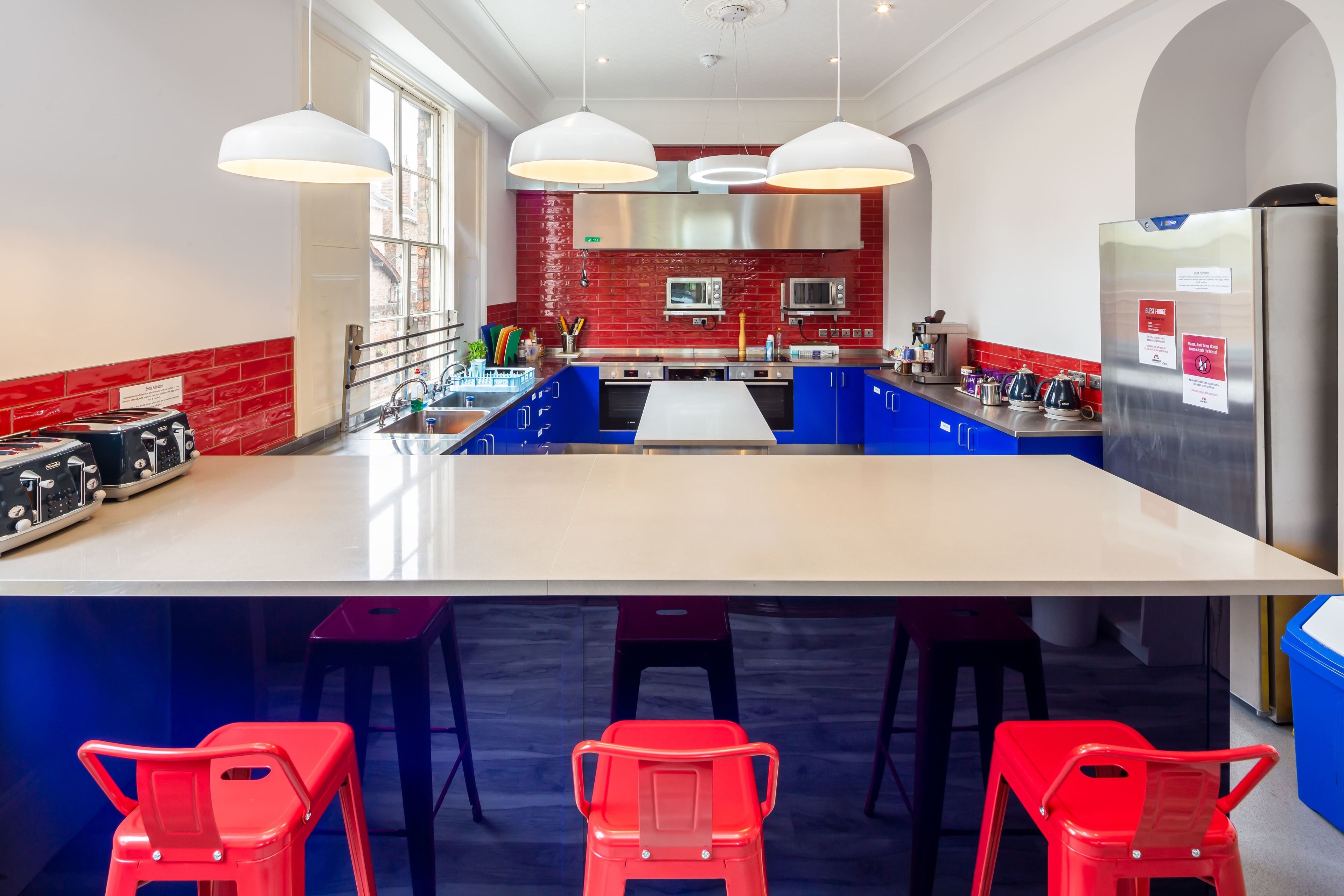 A modern kitchen with a central island, red brick backsplash, stainless steel appliances, and blue bar stools.