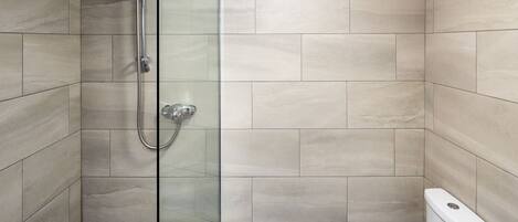 A modern bathroom with a glass shower enclosure, a toilet, and tiled walls.