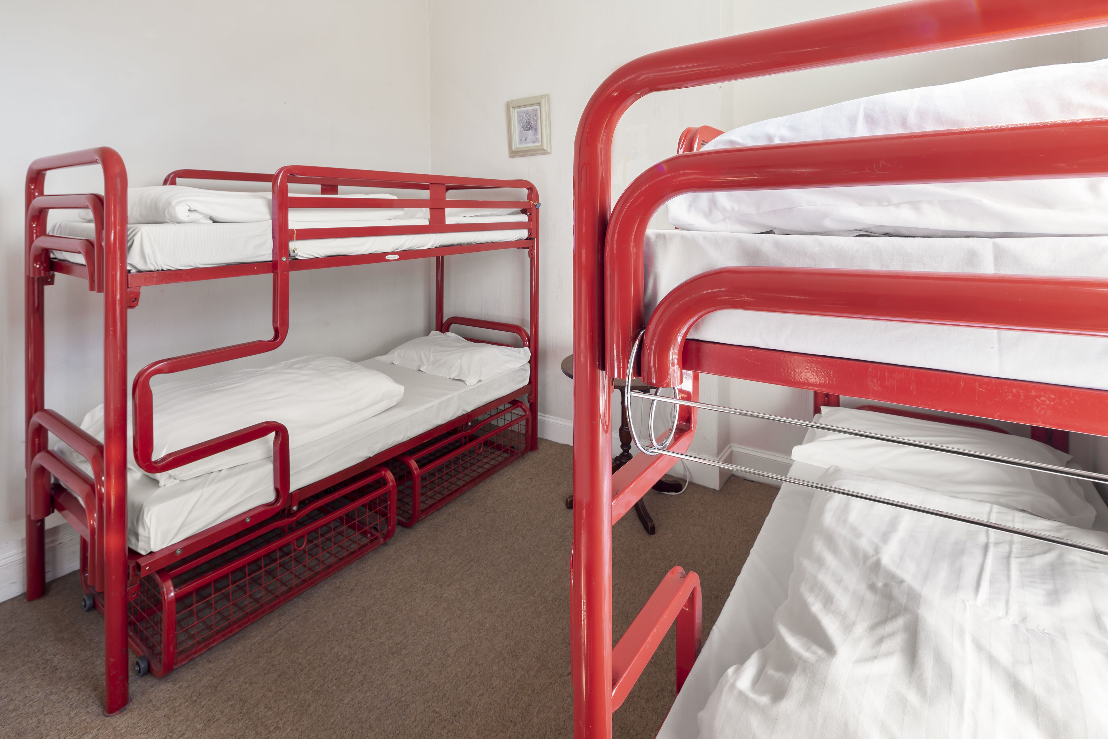 Habitación con literas enmontadas, dos literas rojas, ropa de cama blanca y un pequeño cuadro en la pared.