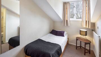 Un dormitorio con cama, mesita de noche con lámpara, ventana con cortinas y espejo en la pared.