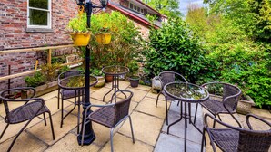 A patio with wicker chairs and tables, surrounded by potted plants and a brick building. - Astor York - Hostel (York)