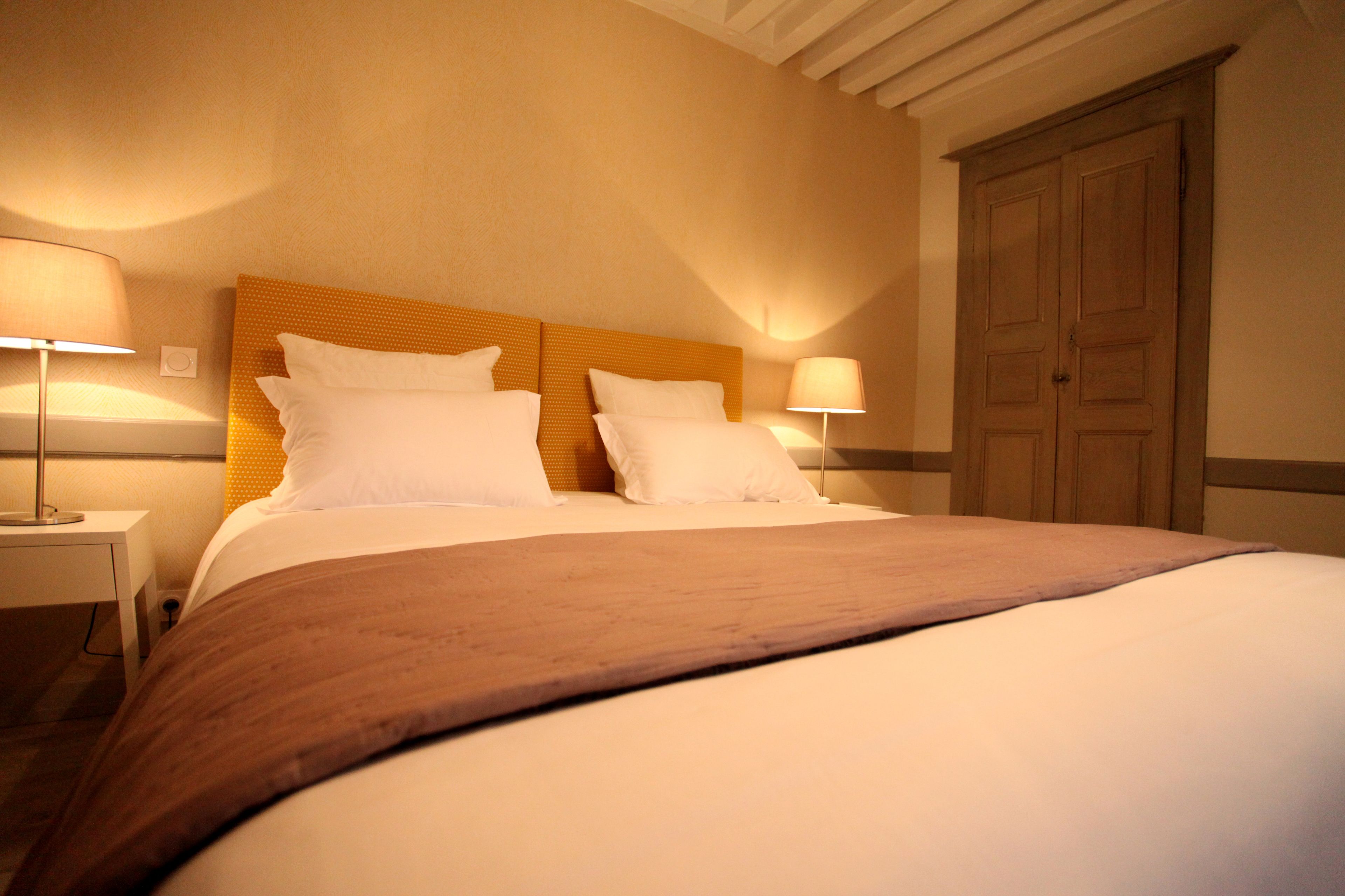 A neatly made bed with a wooden headboard, two bedside lamps, and a wooden wardrobe.