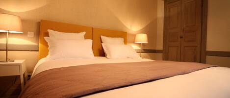 Una cama bien hecha con cabecera de madera, dos lámparas de noche y un armario de madera.
