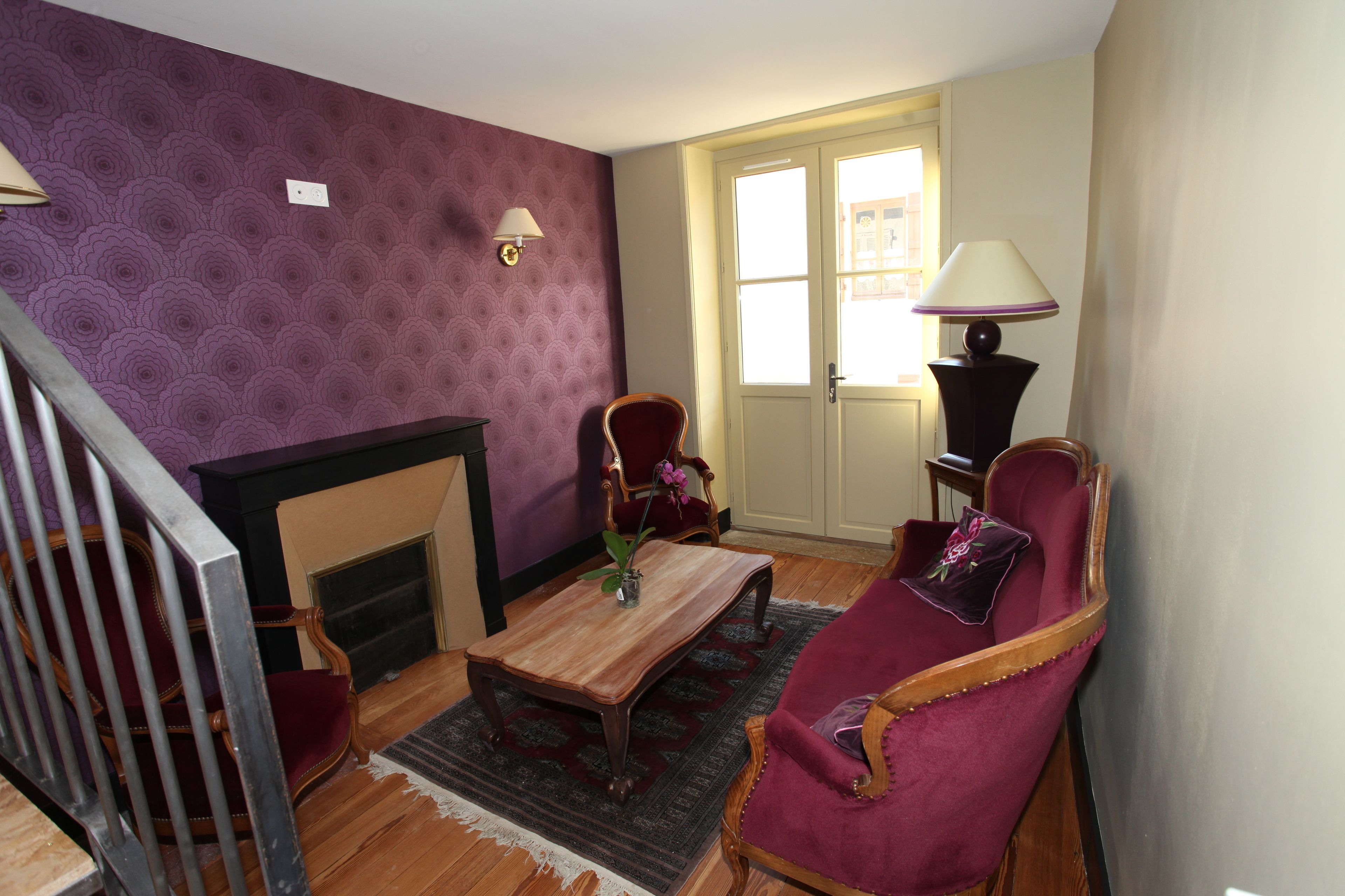 A living room with a fireplace, a wooden coffee table, a red armchair, and a lamp.