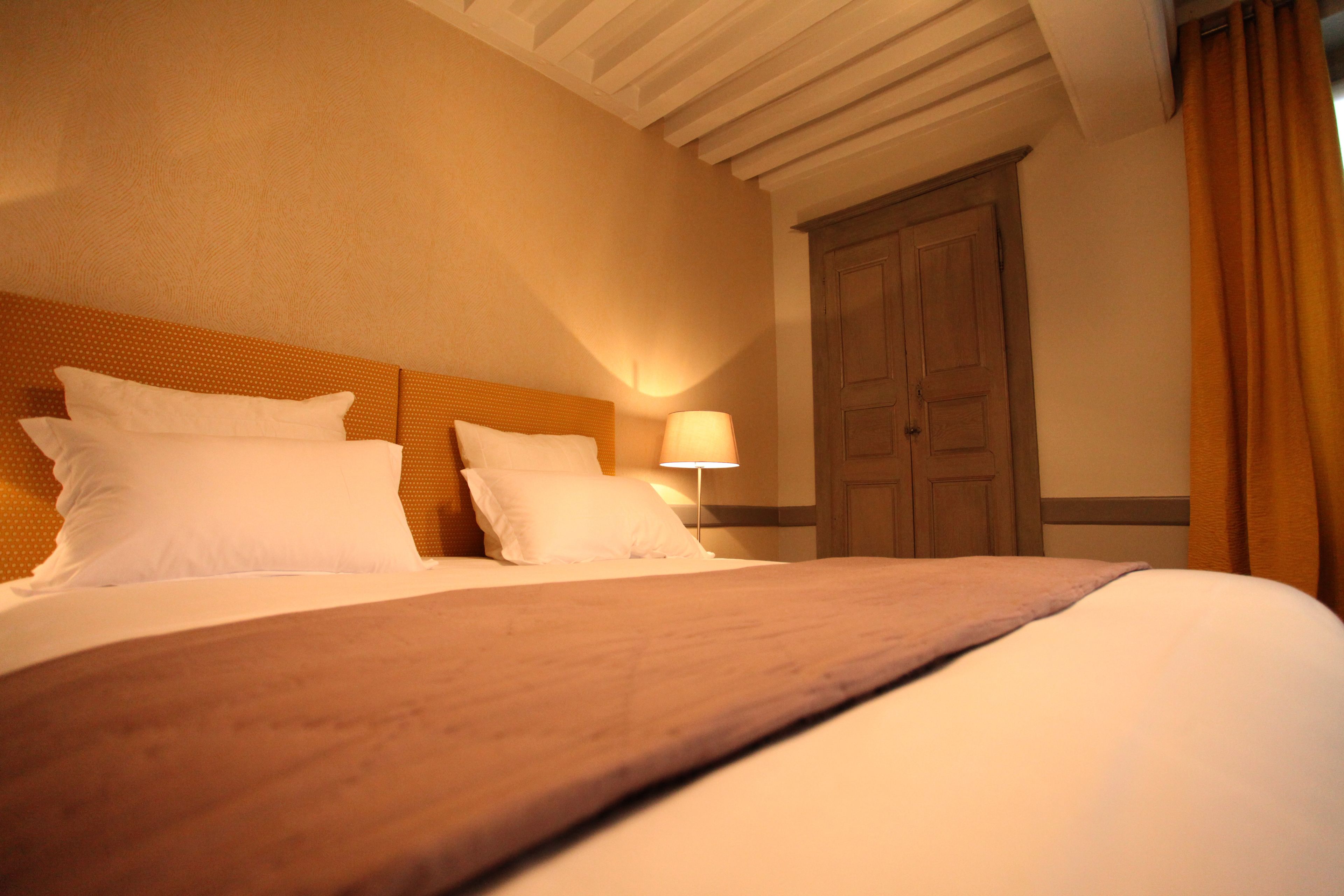 Una habitación de hotel con una cama grande, cabecera de madera, una mesita de noche con lámpara y un armario de madera.