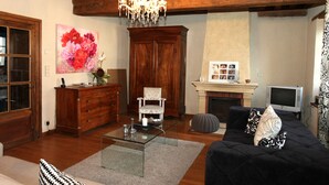 A living room with a wooden ceiling, a chandelier, a fireplace, a television, and a large floral painting. - La Berjotine (Charolles)