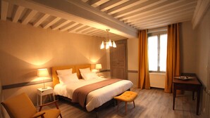 A hotel room with a large bed, a wooden chair, a small table, and a window with curtains. - La Berjotine (Charolles)