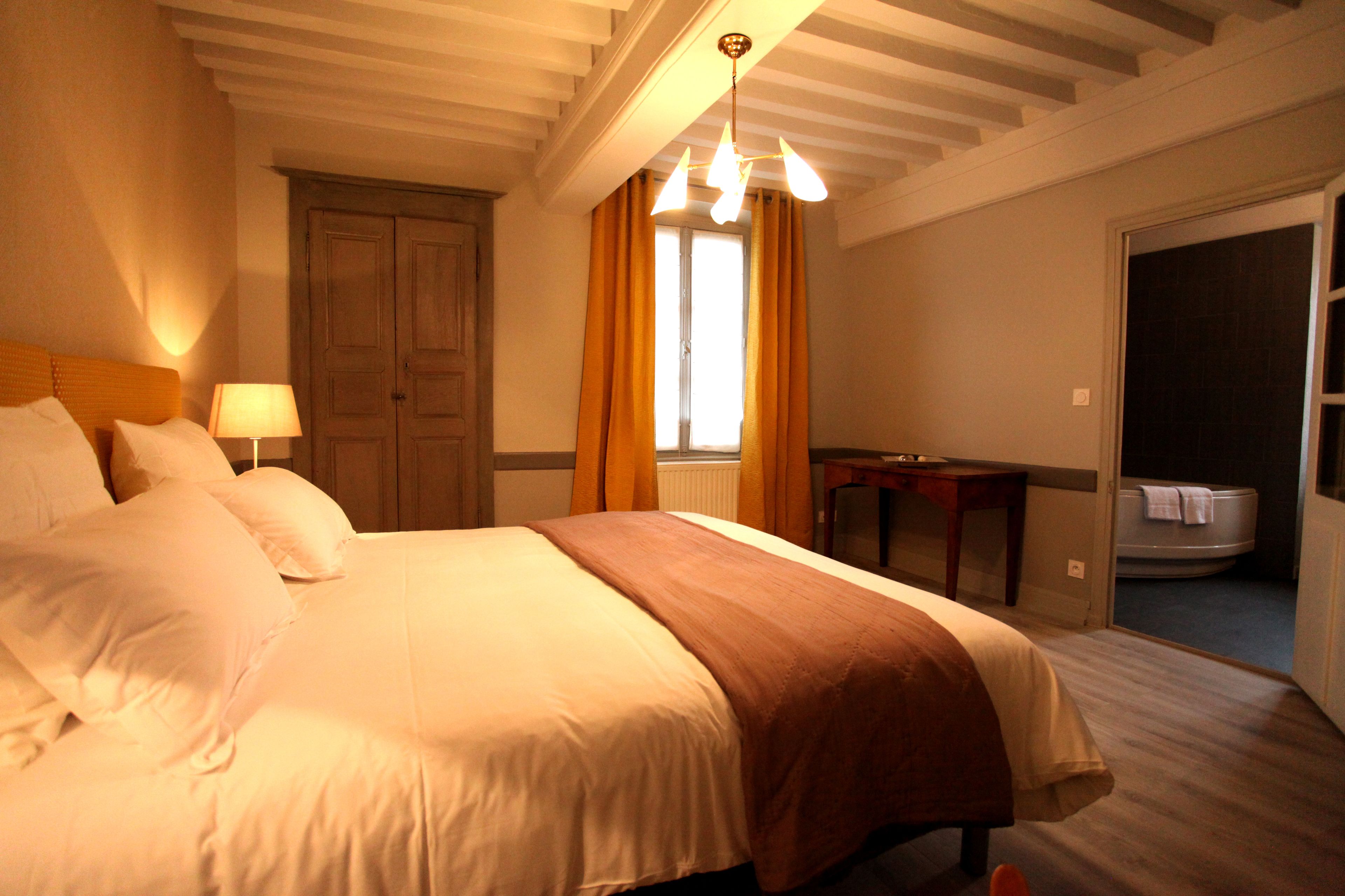 Habitación de hotel con una cama grande, un escritorio y un baño visible a través de una puerta abierta.