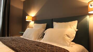 A neatly made bed with a patterned bedspread and two pillows, a headboard with a textured design, and two wall-mounted lamps providing ambient lighting.