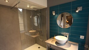 A modern bathroom with a glass-enclosed shower, a white sink, and a blue tiled wall. - La Berjotine (Charolles)