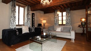 A living room with a black sofa, a grey sofa, a glass coffee table, and a chandelier. - La Berjotine (Charolles)
