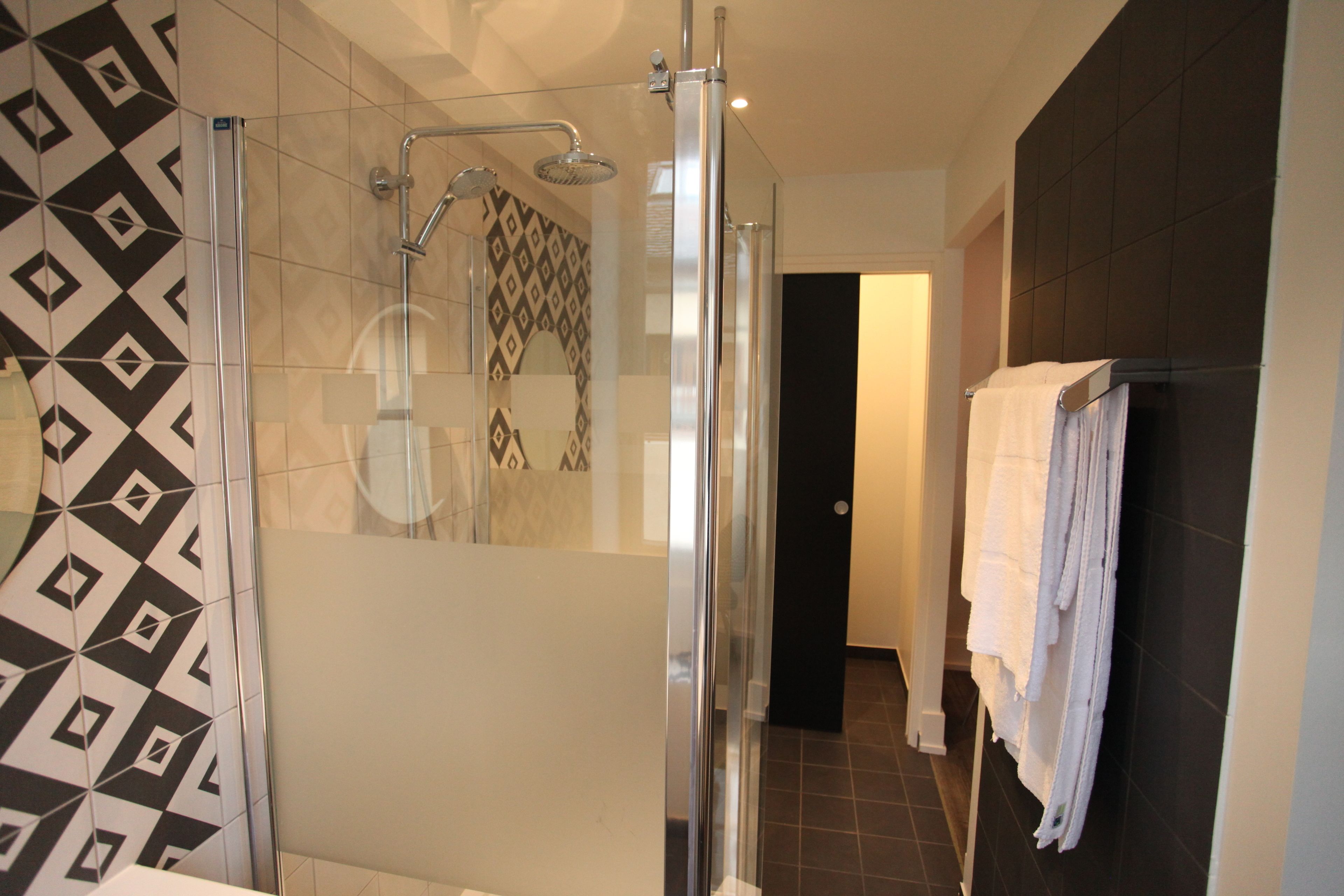 A modern bathroom with a glass-enclosed shower, a patterned wall, and a towel rack.