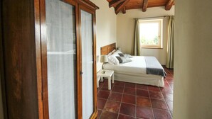 A bedroom with a wooden door, a bed with pillows, a nightstand, and a window with curtains.