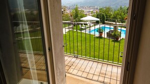 A balcony with a glass door leading to a view of a swimming pool, a lawn, and distant mountains.