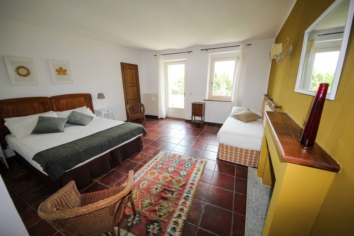 A bedroom with a large bed, a chair, a small table, and a window.