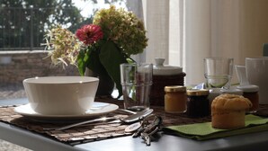 A dining table with a white bowl, a glass of water, a glass of juice, a muffin, and a vase with flowers.