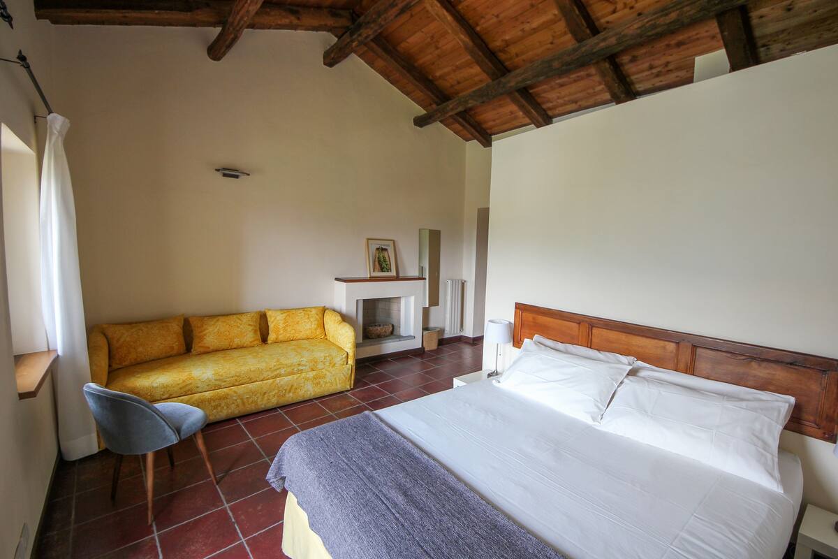 A bedroom with a bed, a sofa, a chair, and a fireplace.