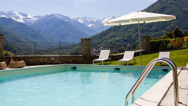A pool with a view of snow-capped mountains, lounge chairs, and an umbrella.
