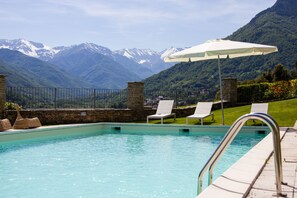 A pool with a view of snow-capped mountains, lounge chairs, and an umbrella. - Cascina del Forte (Torre Pellice)