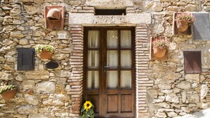 A stone building with a wooden door, potted plants, and a number '10' sign. - Le Dame del Borgo (Sassetta)