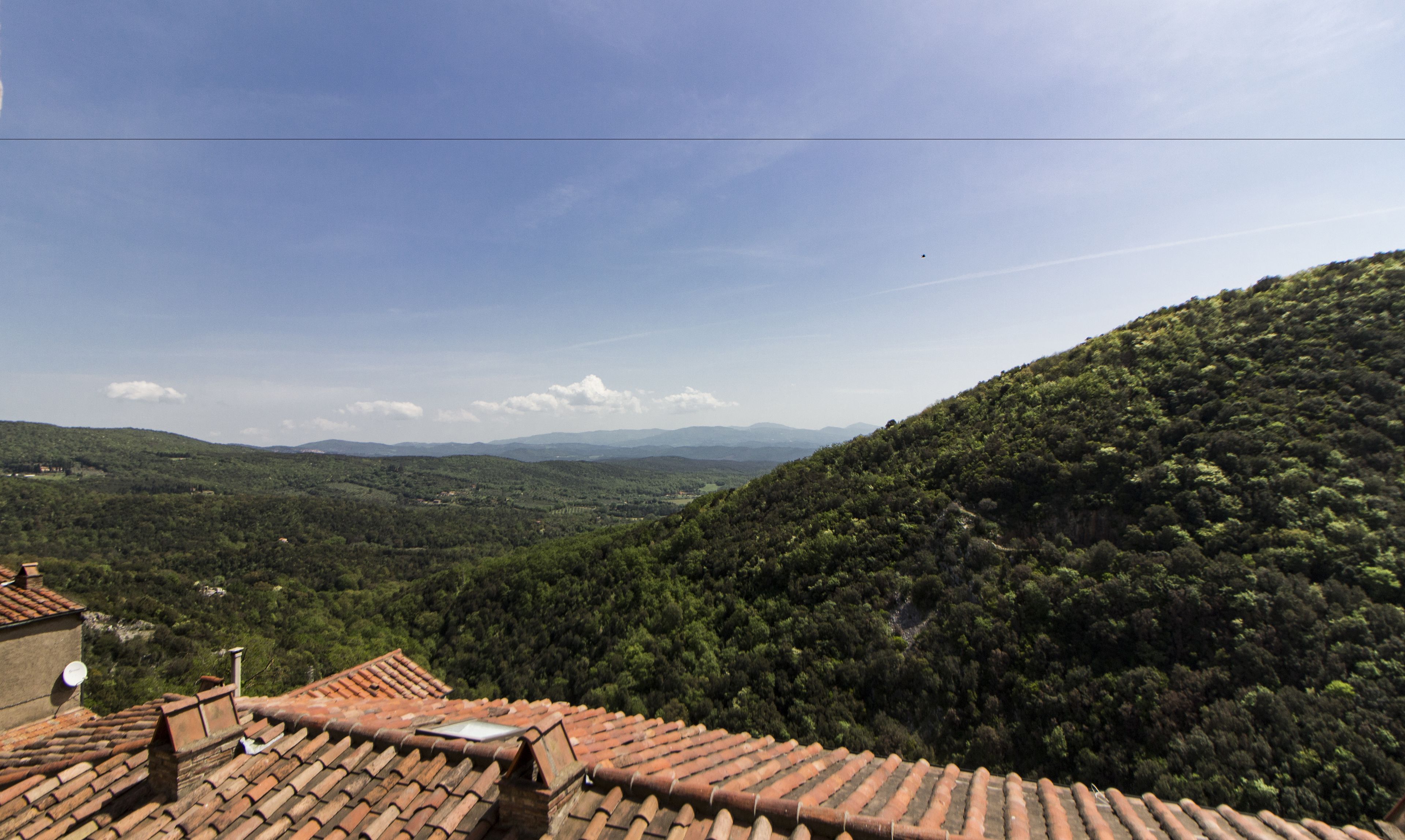 A view from a terracotta-tiled roof overlooking a lush, green valley with distant mountains.