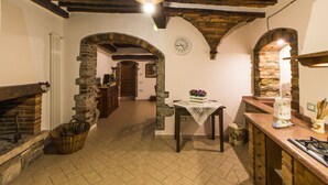 A rustic kitchen with exposed brick walls, a wooden ceiling, and a stone archway leading to another room. - Le Dame del Borgo (Sassetta)