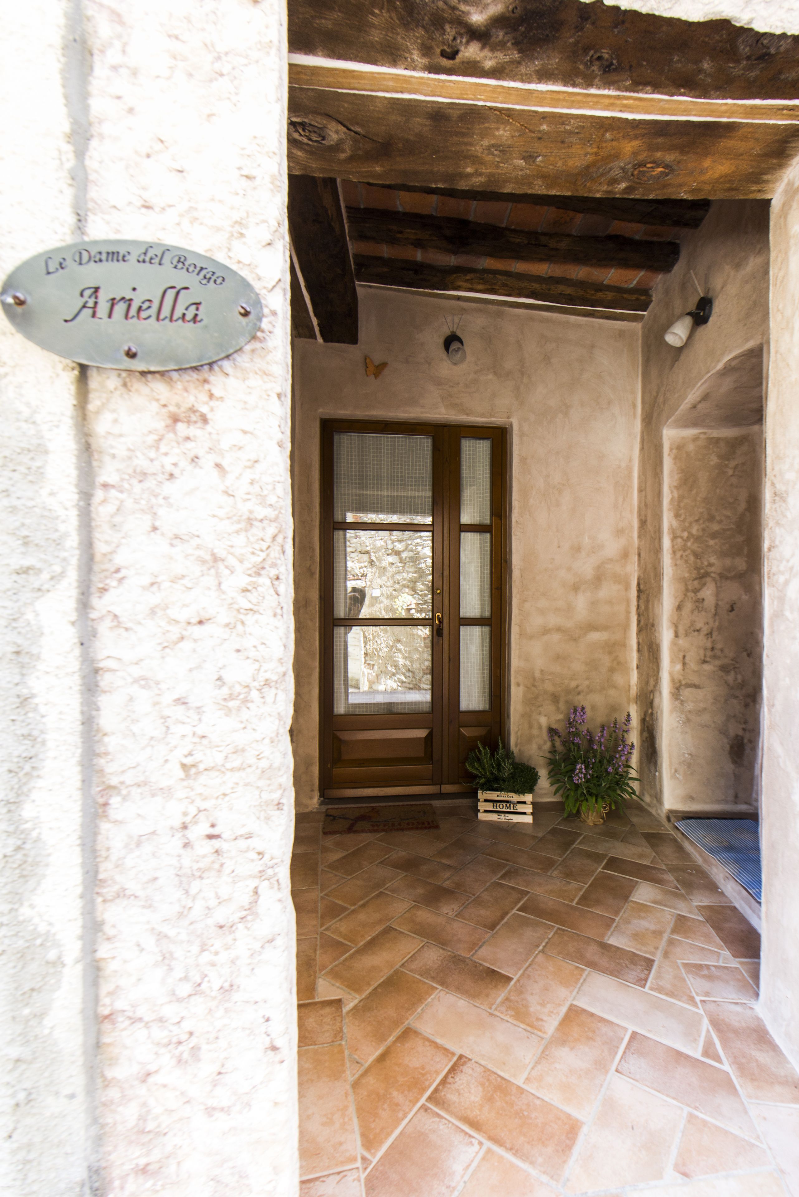 Une entrée rustique avec un sol carrelé, une porte en bois et une enseigne indiquant « Le Dame del Borgo Ariella ».