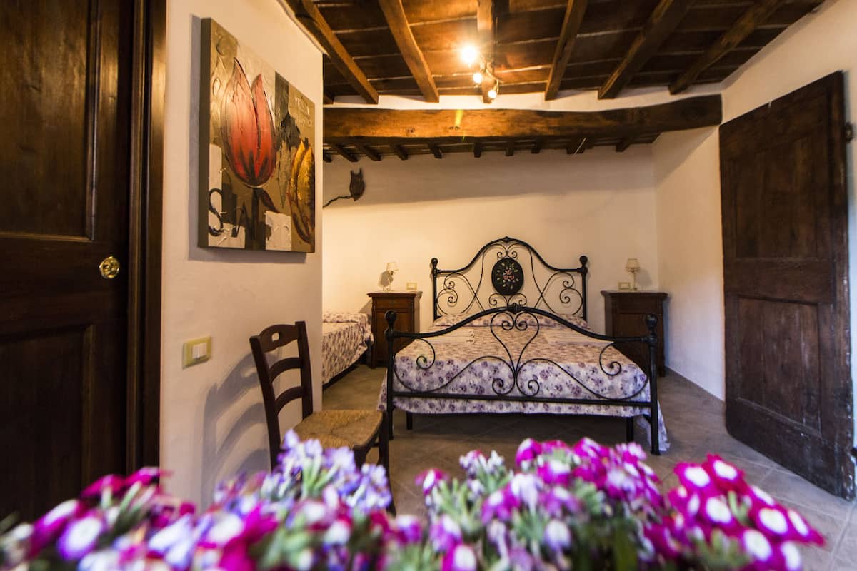 A bedroom with a bed, a chair, a nightstand, a wall-mounted lamp, and a door.