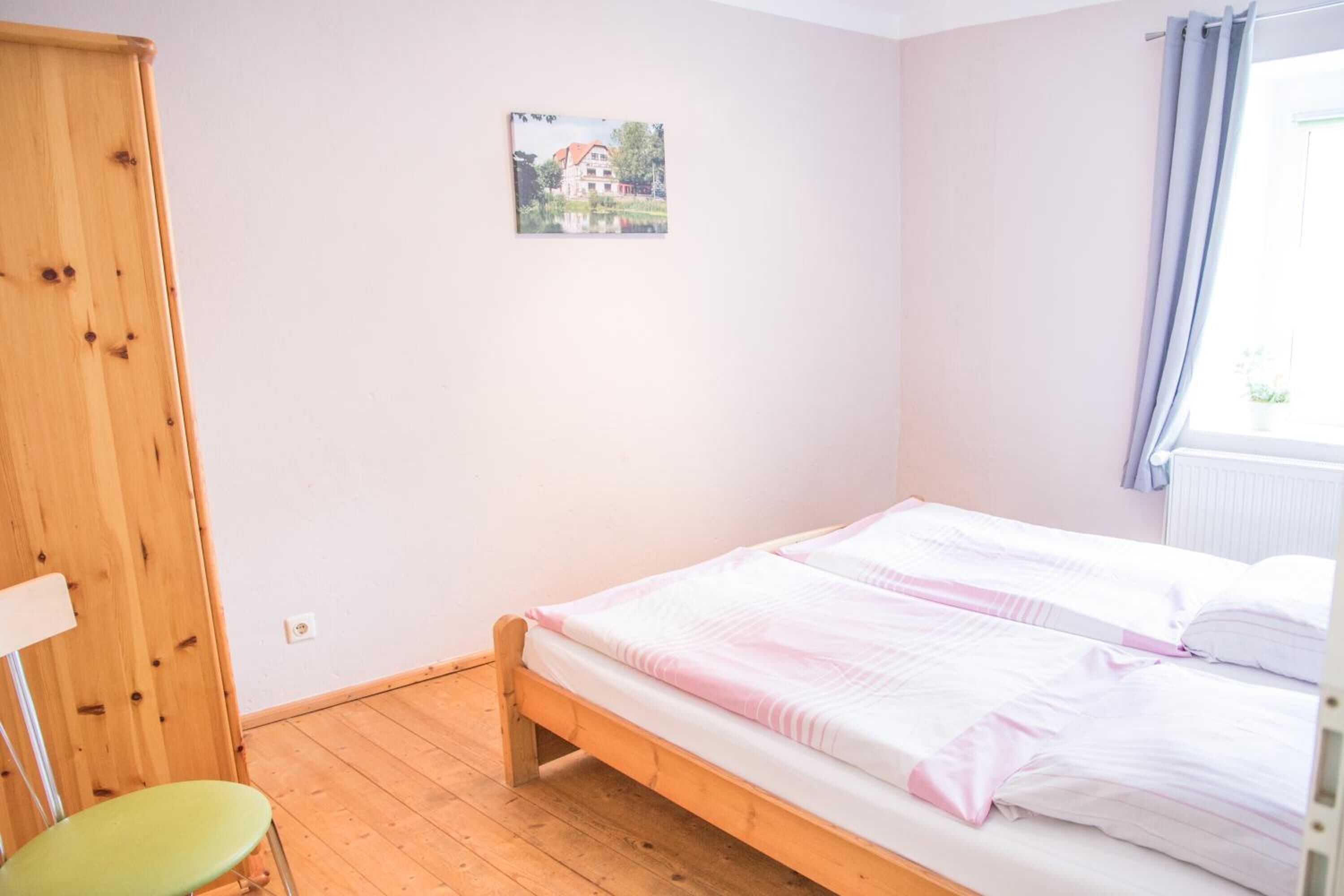 A bedroom with a wooden bed, a green chair, and a small picture on the wall.