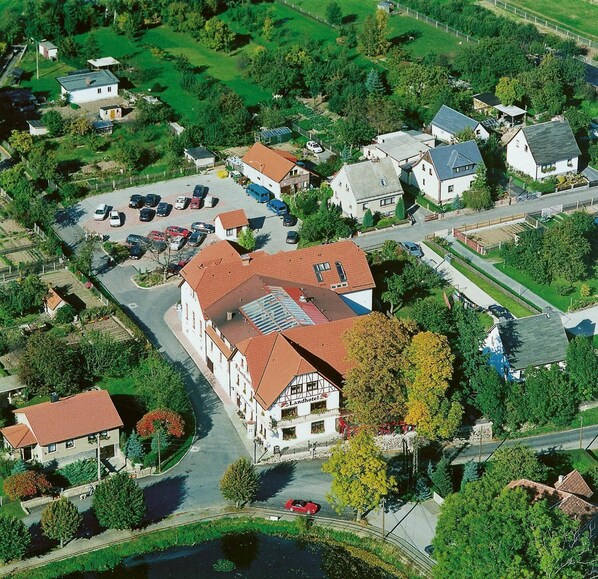 An aerial view of a hotel with a red-tiled roof, surrounded by greenery and a parking lot. - Landhotel Reiterhof Schumann (Triptis)