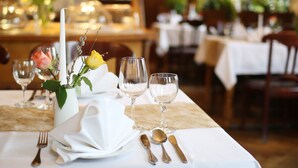 Een eettafel, gedekt met een witte tafeldoek, bestek en een vaas met bloemen.