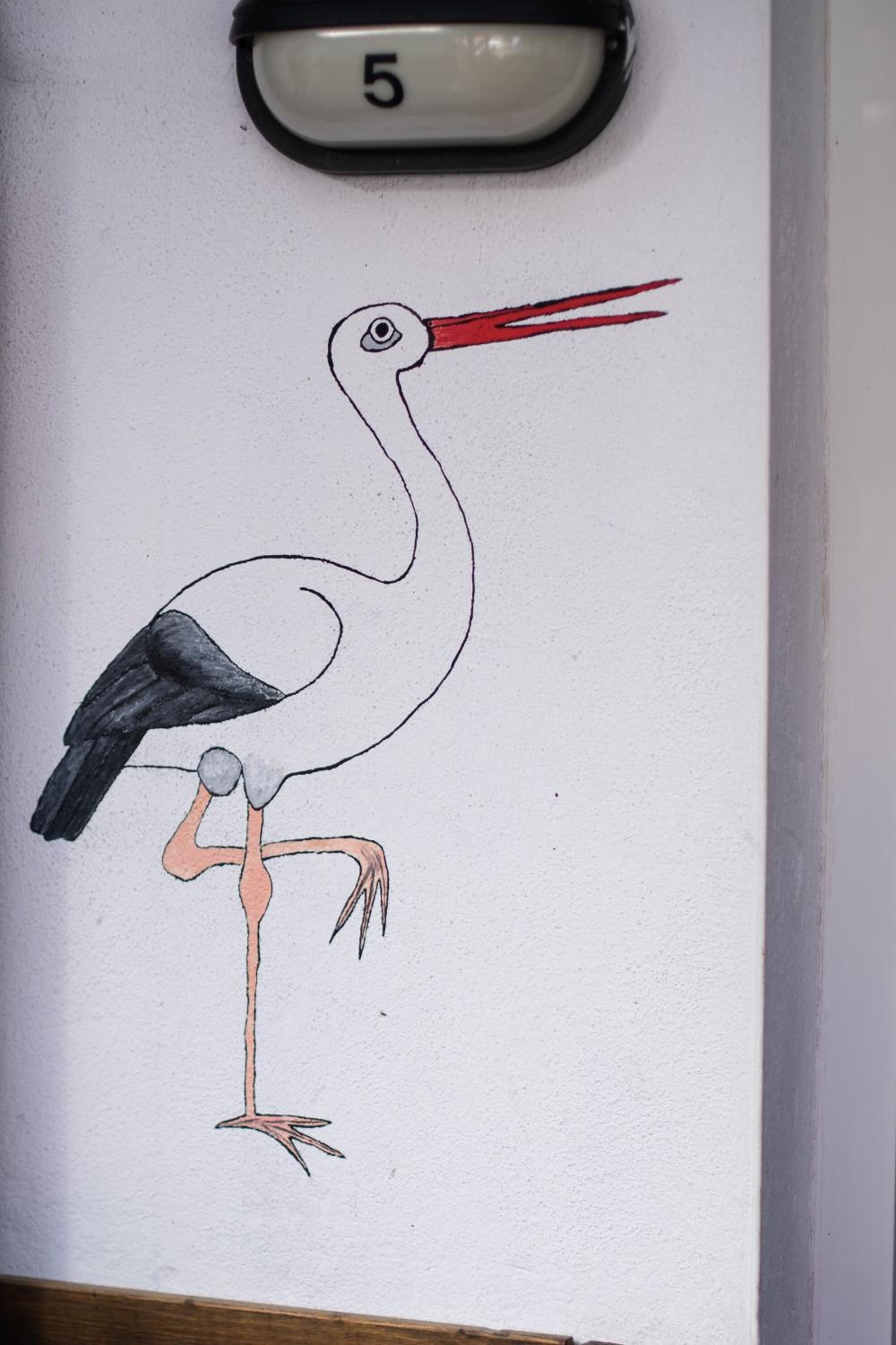 A wall with a stork illustration and a doorbell labeled "5".