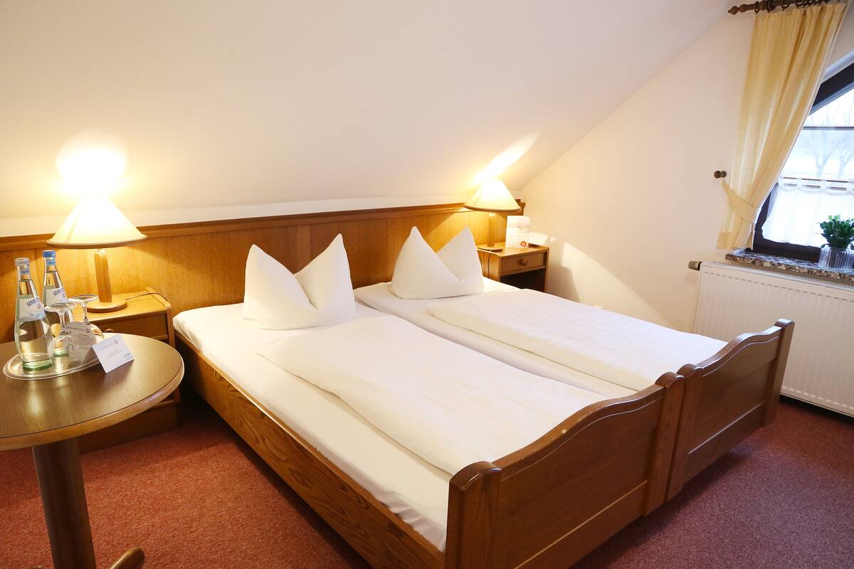 A hotel room with a wooden bed, two bedside tables, a small round table, and a window with curtains.