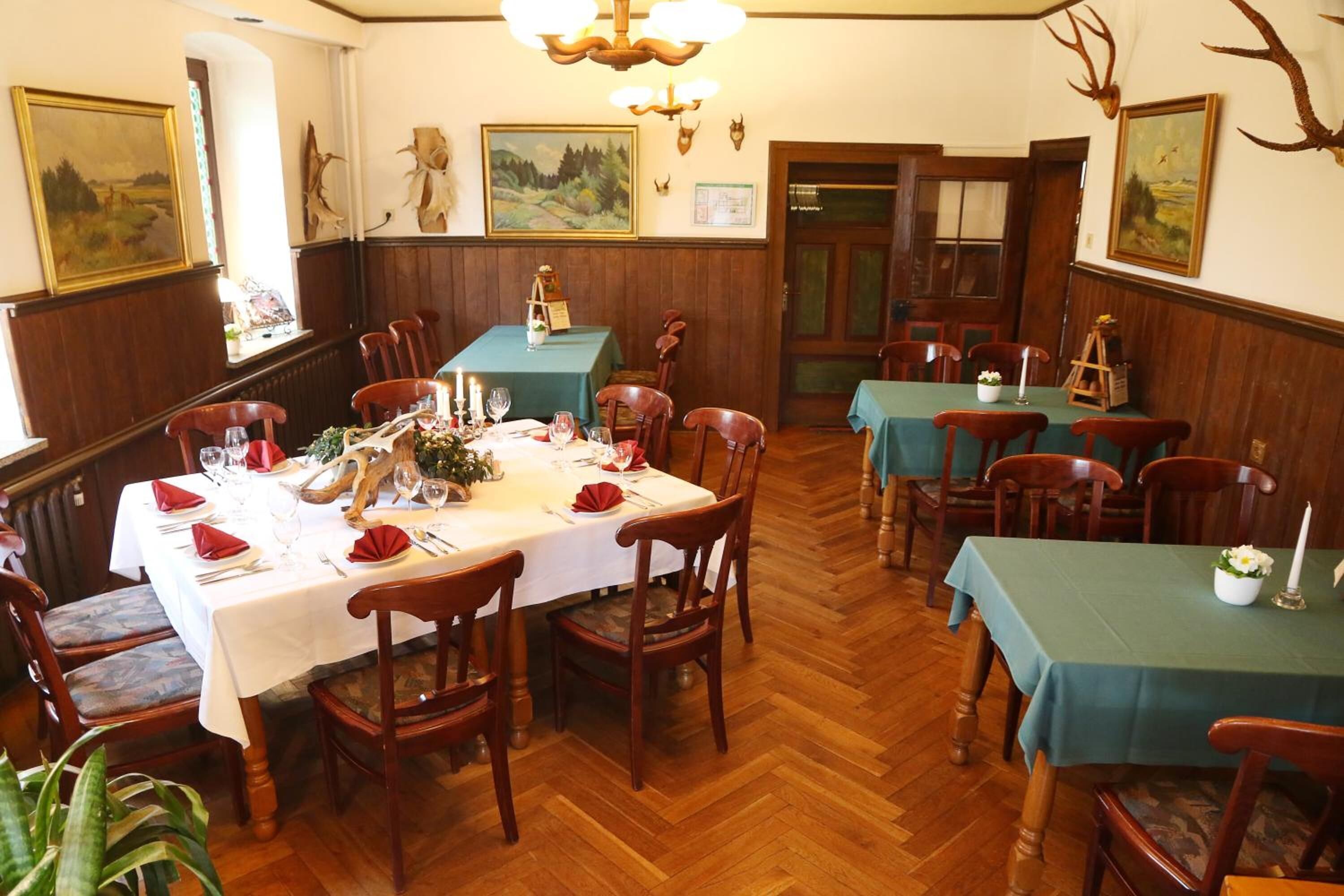 Un comedor con varias mesas dispuestas para comer, sillas de madera y una araña.